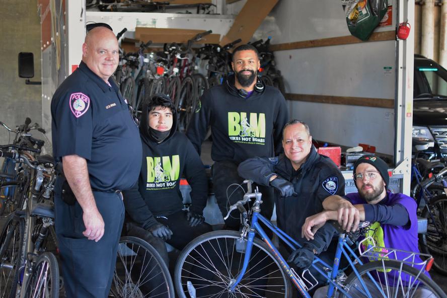 Five TUPD officers posing in front of a white truck with the backend open and revealing many bicycles.