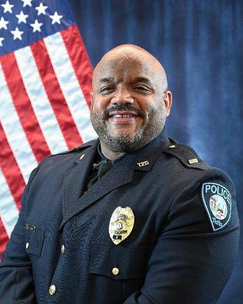 A police officer smiling in front of an American flag