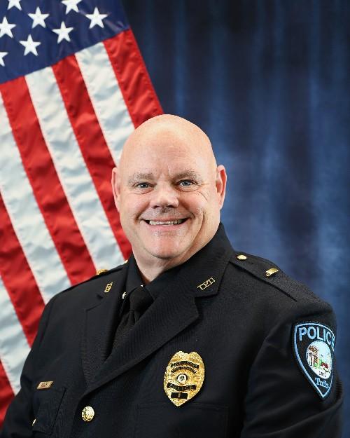 A police officer smiling in front of an American flag