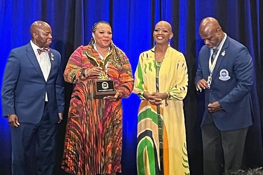 A group of people stand on a stage, with a woman holding an award
