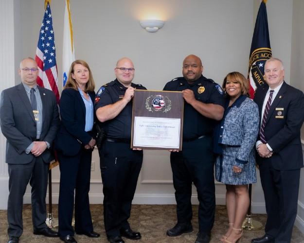A group of people and police officers stand holding a plaque in the center