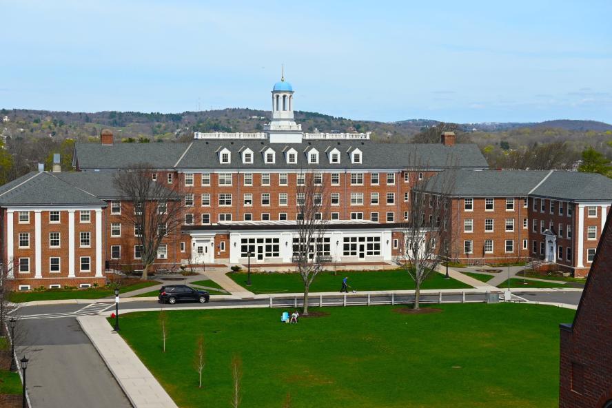 An academic building with a green lawn in front of it and hills behind it