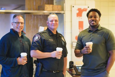 Group posing with police officer holding coffee cups