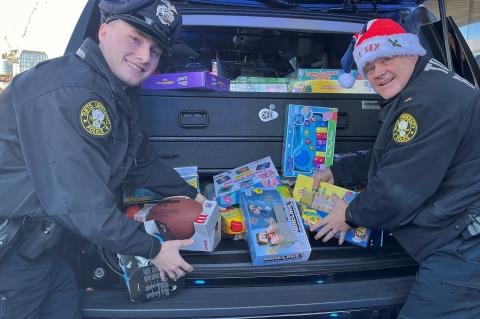 Two TUPD officers smiling and packing toys in a SUV trunk.
