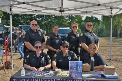 Seven TUPD officer sitting at a table booth outside posing and smiling.